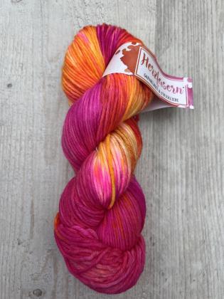 „Handgefärbter Strang in Pink-, Orange- und Gelbtönen, kräftig und warm, fotografiert auf hellem Holzuntergrund mit Herzfasern-Etikett.“